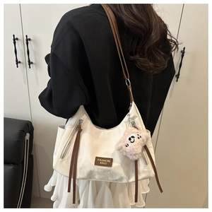 Detail of off-white shoulder bag with brown leather strap and pink plush charm accessory