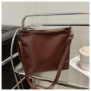 Détail d'un sac seau marron avec bandoulière réglable et boucle en argent sur étagère