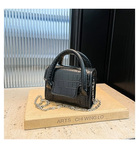Close-up of black crocodile-embossed mini handbag with silver chain on artsy books
