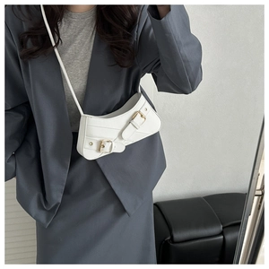 Detailed view of the white saddle bag with asymmetrical contour and gold buckle closure