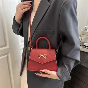 Fashionable red crossbody bag with golden bow clasp carried by a model in a grey suit