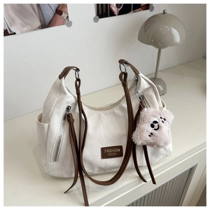 Close-up of white pleated tote bag with plush bear charm and brown leather brand patch