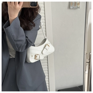 Close-up of white faux leather saddle bag featuring elegant gold metal buckles and slim strap