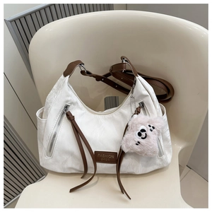 Detail of white nylon tote with brown leather accents and plush bear charm on a chair