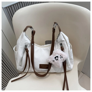 Close-up of white faux leather tote with brown straps, fringe detail and plush charm