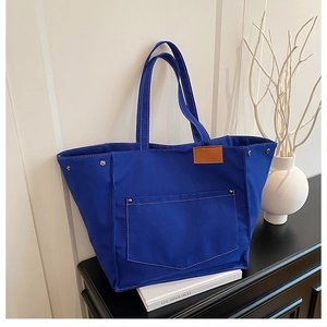 Detail of Klein blue canvas tote bag with leather label and studs on a bookshelf