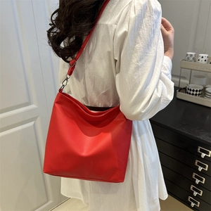 Sac seau rouge vif à plis avec crochets noirs porté par un mannequin en robe blanche