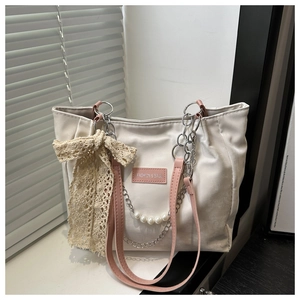 Detail of beige tote bag with pink straps, pearl chain, and large lace bow accessory
