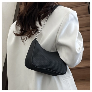 Detail of black corduroy crescent bag with silver chain strap on a white blazer