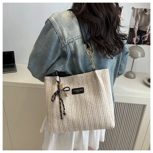 Detail showing handwoven beige straw tote with black leather brand tag and contrast stitching
