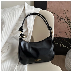Minimalist black leather underarm bag with gold logo hanging on a beige chair
