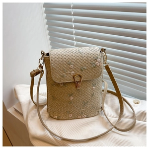 Dettaglio di ricamo floreale su borsa a secchiello beige con chiusura girevole dorata