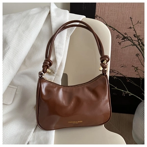Detailed view of dark brown glossy leather shoulder bag with knotted strap and gold hardware