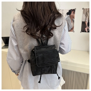 Détail du mini sac à dos noir à texture plissée porté par un mannequin en intérieur