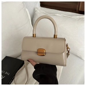 Close-up of beige glossy leather handbag with vintage gold buckle on a soft white bed
