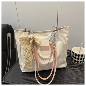 Detail of canvas tote bag featuring cream lace bow, pearl chain and pink leather label