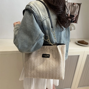 Minimalist beige woven straw tote bag with black leather straps and brand logo patch