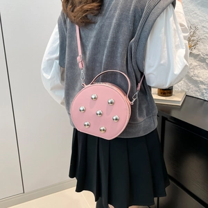 Pink semi-circle crossbody bag with silver studs worn by a model in modern setting