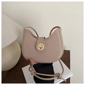 Close-up of beige crescent bag with golden twist lock and knotted strap detail