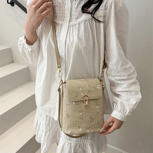 Straw bucket bag with floral embroidery and gold metal clasp on a white lace outfit
