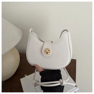 Detail of white leather crescent hobo bag featuring a gold round twist lock on wooden desk