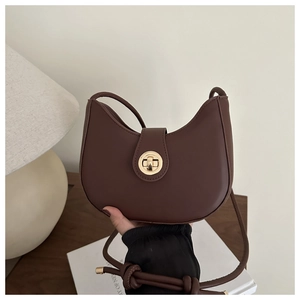 Detail of a brown leather crescent bag featuring a golden twist lock and knotted strap