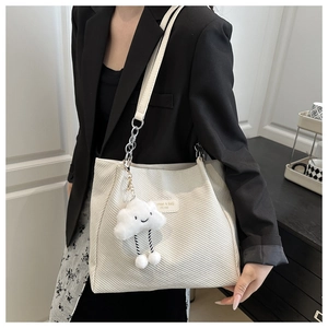 Detail of white corduroy tote bag featuring a metal chain strap and plush cloud charm