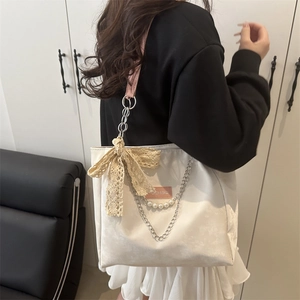 Off-white corduroy tote bag with lace bow and pearl chain shown on a model
