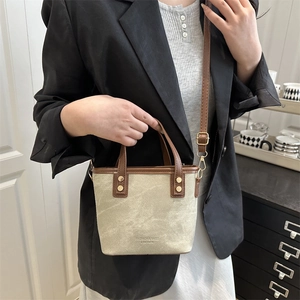 Canvas and leather bucket bag with top handle and adjustable shoulder strap worn by model