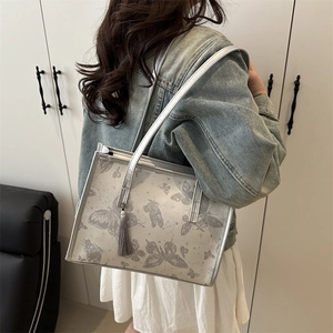 Minimalist silver tote bag with butterfly print and tassel detail shown on shoulder