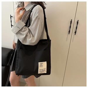 Detail of black canvas tote bag with shoulder strap and stylish text patch on the corner