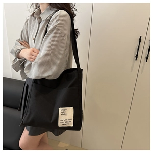 Detail of black canvas tote bag featuring dual front pockets and decorative woven labels