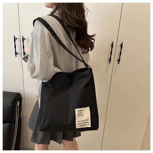 Detail shot of a black canvas tote bag with a text patch worn by a model in a striped shirt