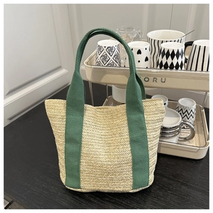 Detail of woven straw tote bag with green fabric straps on a clean white shelf