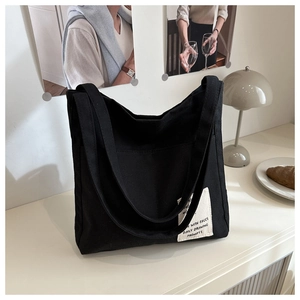 Close-up of black canvas tote bag with white woven label on a minimalist desk set