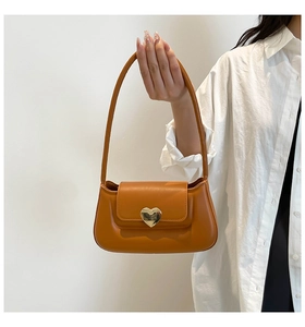 Detail of the golden heart-shaped clasp on a brown leather shoulder bag with smooth texture