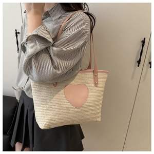 Détail du sac cabas tissé avec un patch cœur en cuir rose et fixations de sangle à rivets