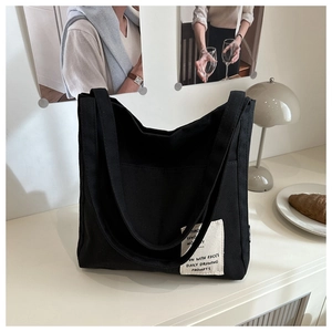 Detail shot of black canvas tote bag with white patch on a cozy desktop setting