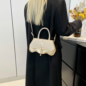 Sac à main doré pailleté avec base ondulée et logo SN porté par un mannequin mode