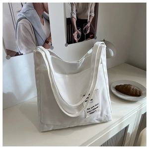 Detail of white canvas tote bag with Sunday text patch and side pocket on a desk