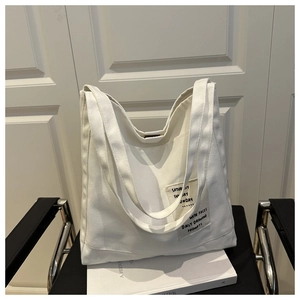 Detail of white canvas tote bag with black minimalist typography on a white prop book
