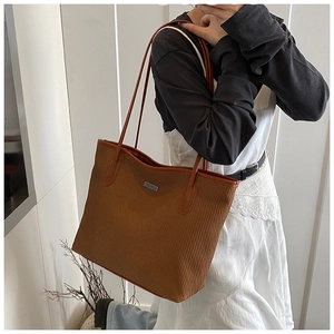 Close-up of brown woven tote bag featuring a minimalist metal plaque and fine texture