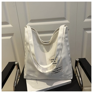 Detail of white canvas tote bag with daily lettering patch and spacious open-top design