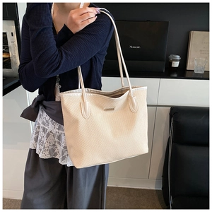 Detail of cream woven tote bag featuring leather handles and metal logo plate on a model