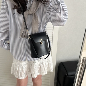 Sac seau chic en cuir noir avec boucle dorée, porté par un mannequin en tenue décontractée