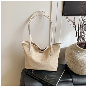 Artistic detail of a beige woven tote bag resting on black books with minimalist decor