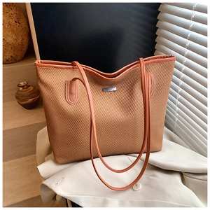 Detailed macro of a woven tote bag with brown leather trim and metal logo on a blazer