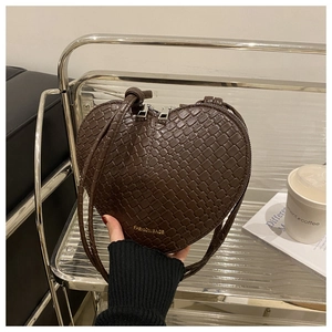 Detail of dark brown heart-shaped woven bag with gold logo on a glass display shelf