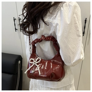 Détail du sac croissant bordeaux brillant avec poignée plissée et breloque perle nœud