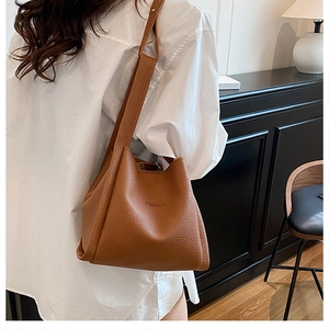 Detail of caramel lychee leather bucket bag with Fashion text worn by a model